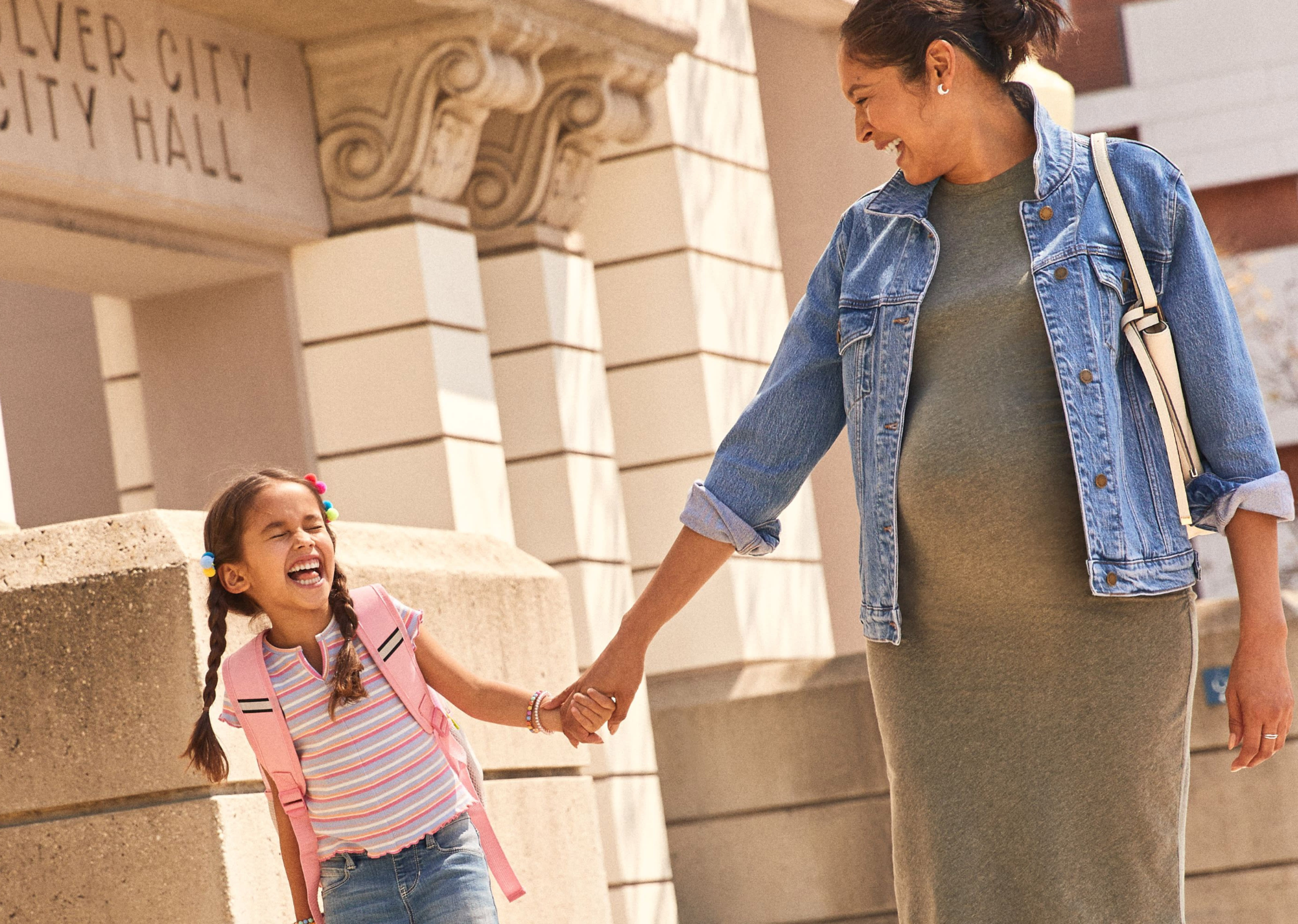 A pregnant woman holds hands with her young daughter.