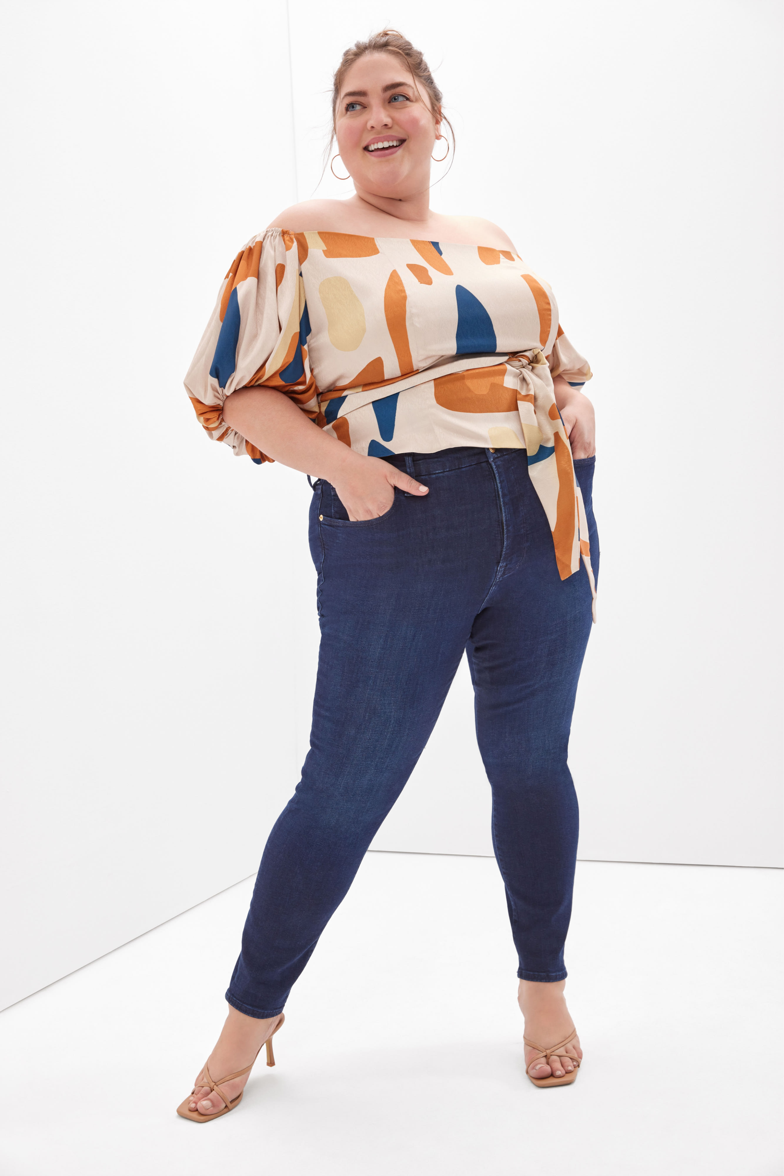 Plus-size model wearing women’s Stitch Fix clothing, including colorful patterned sweater and dark wash skinny jeans.