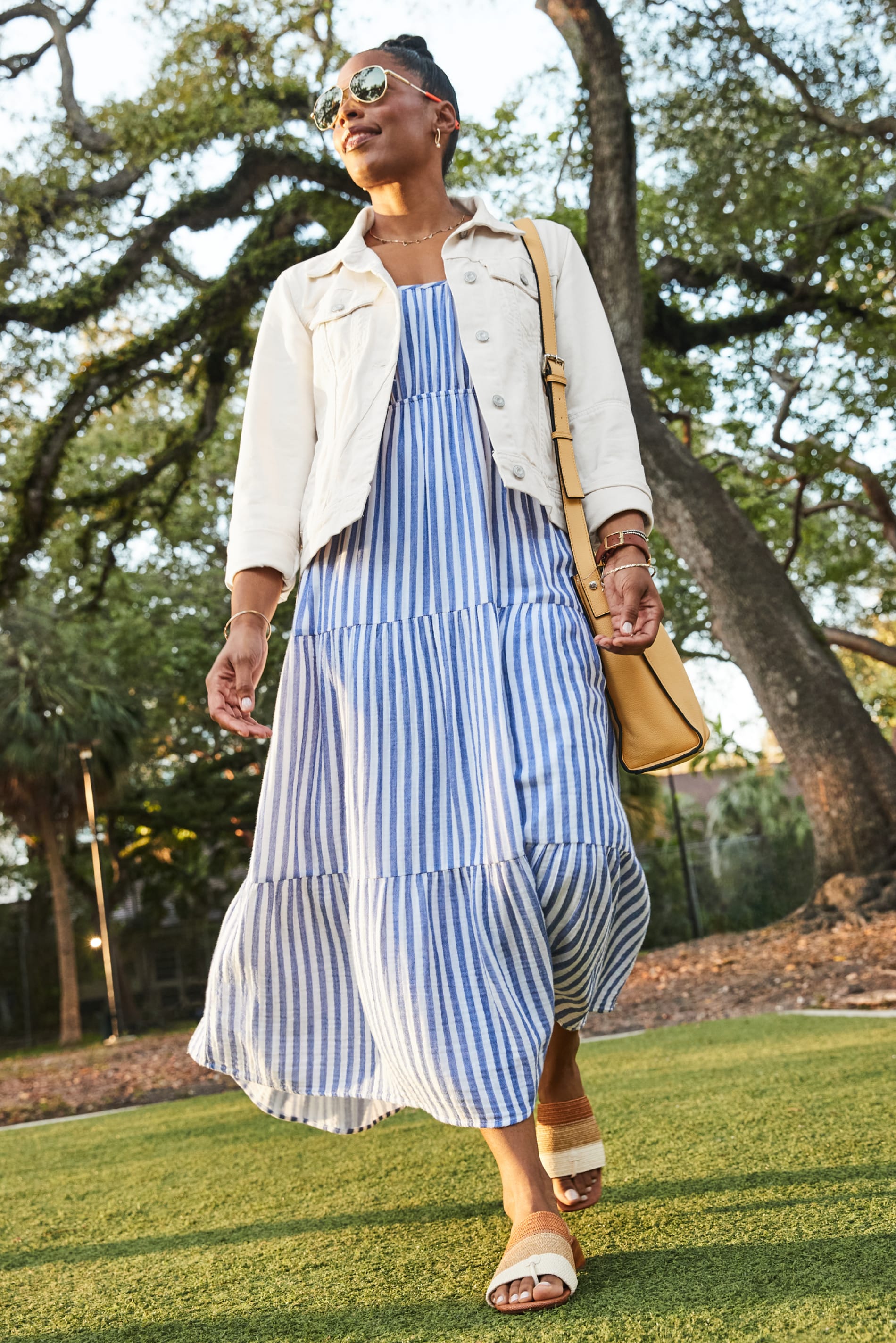 Model wearing Stitch Fix women’s clothing including blue dress, white jean jacket and yellow purse.