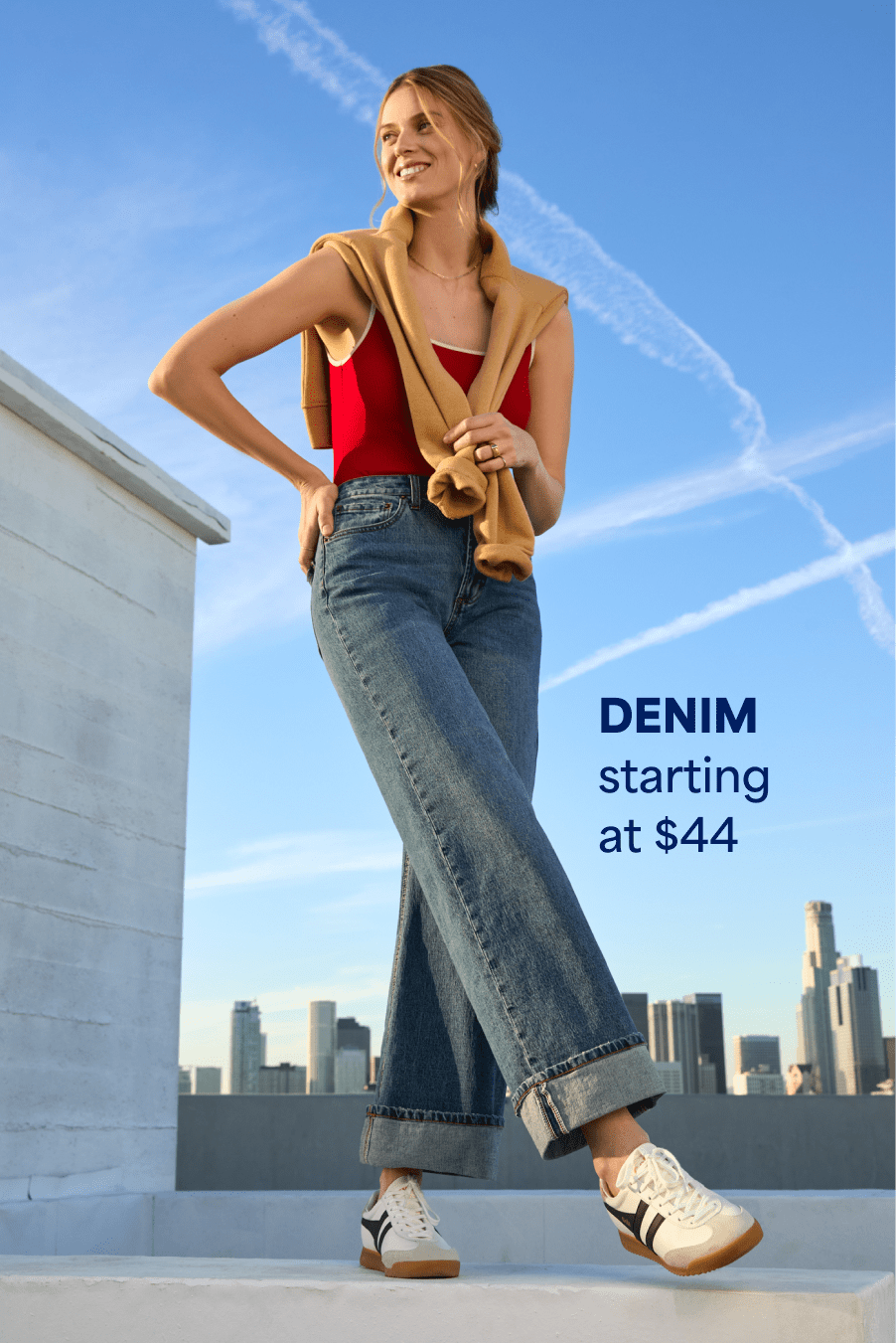 Model wearing Stitch Fix women’s clothes including tan sweater, red tank top, wide-leg jeans and white sneakers. Text reads: DENIM starting at $44.