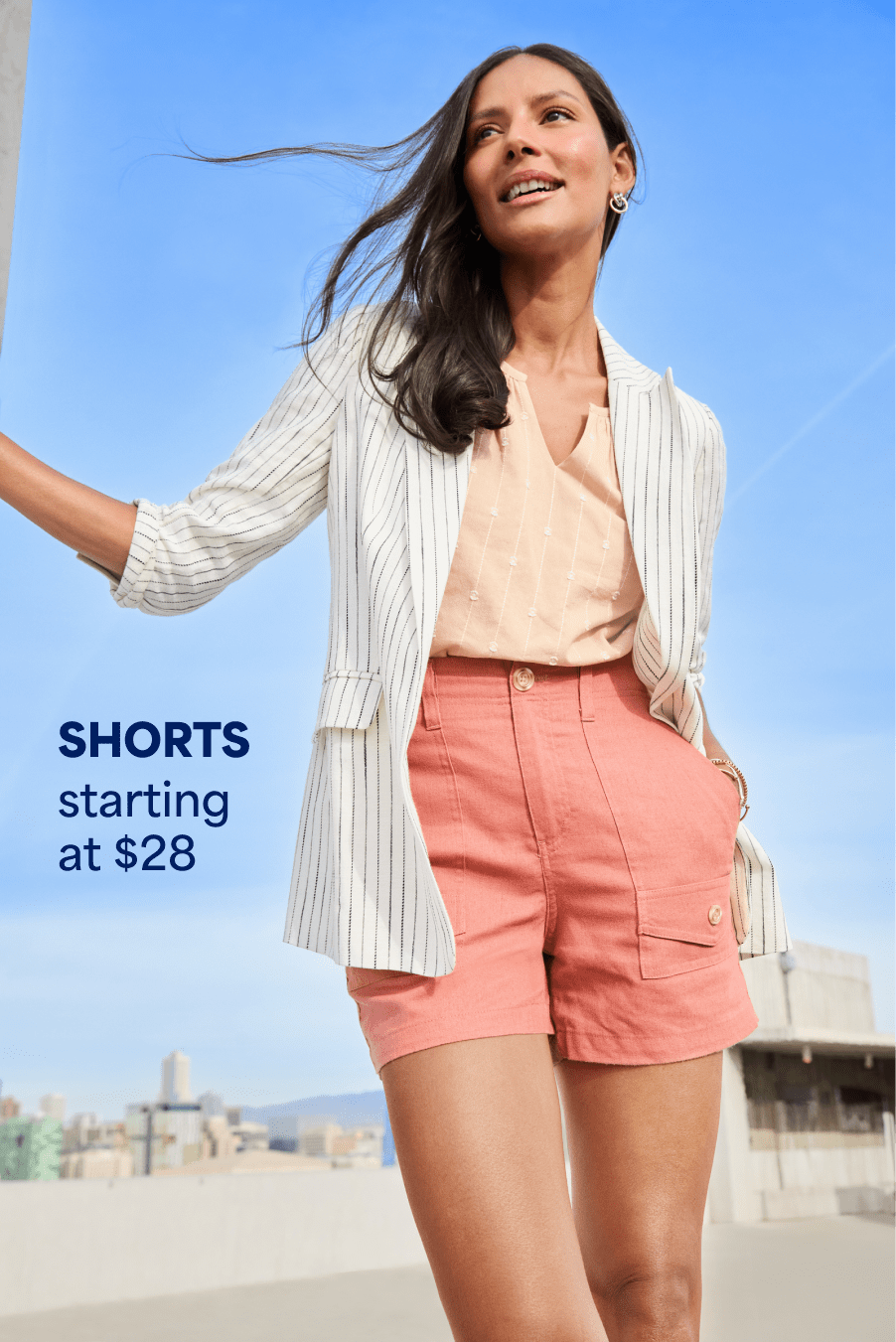 Model wearing Stitch Fix women’s clothes including light blazer, peach blouse, coral shorts. Text reads: SHORTS starting at $28.
